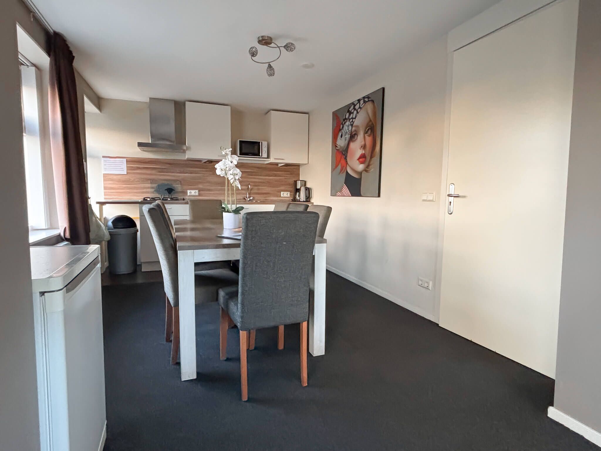 A modern kitchen with a dining area, white cabinets, a microwave, and a decorative painting.