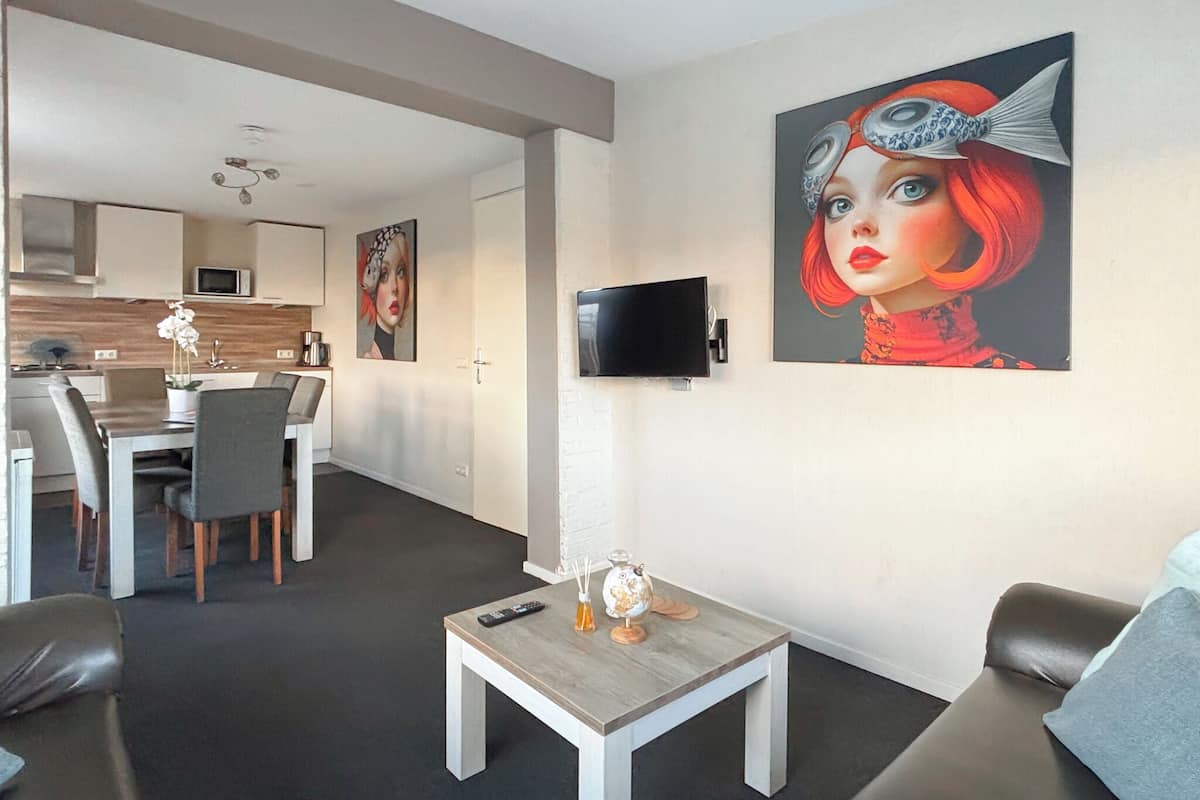A modern living room with a dining area, a kitchen in the background, and a large painting on the wall.