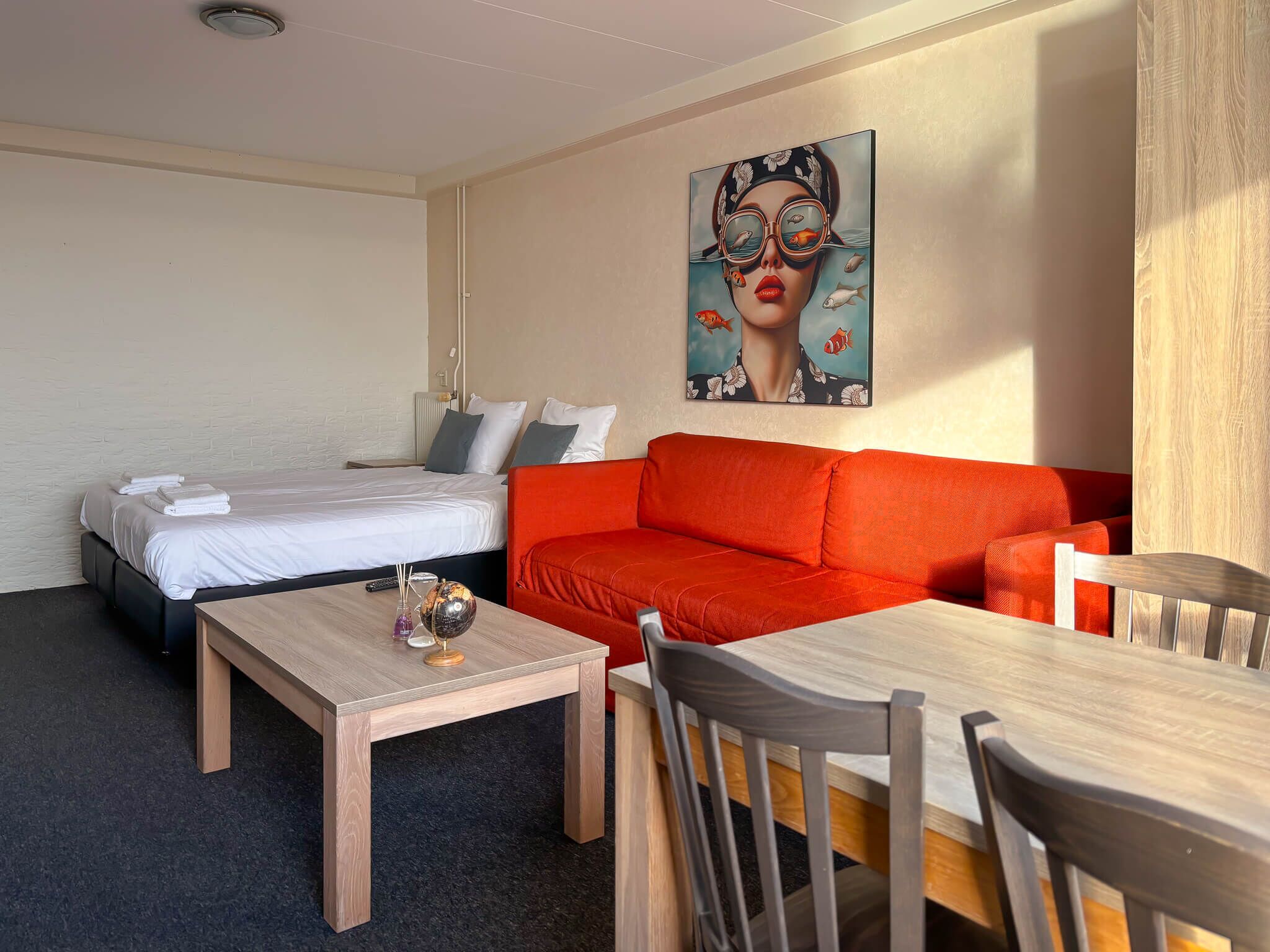 A hotel room with a bed, a red sofa, a wooden table, and a painting on the wall.