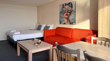 A hotel room with a bed, a red sofa, a wooden table, and a painting on the wall.