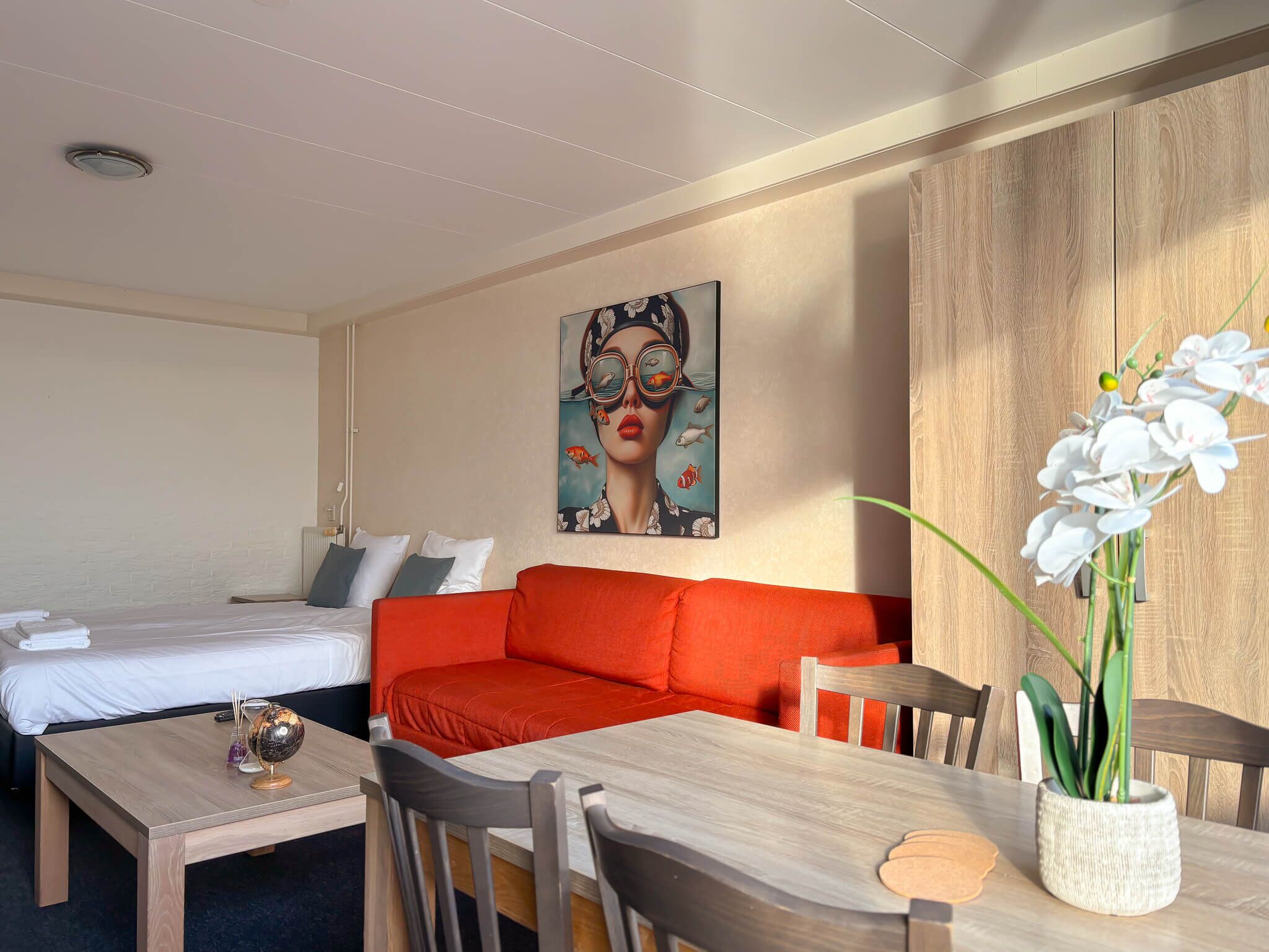 Ein Hotelzimmer mit einem Bett, einer roten Couch, einem Holztisch und einem Bild an der Wand.