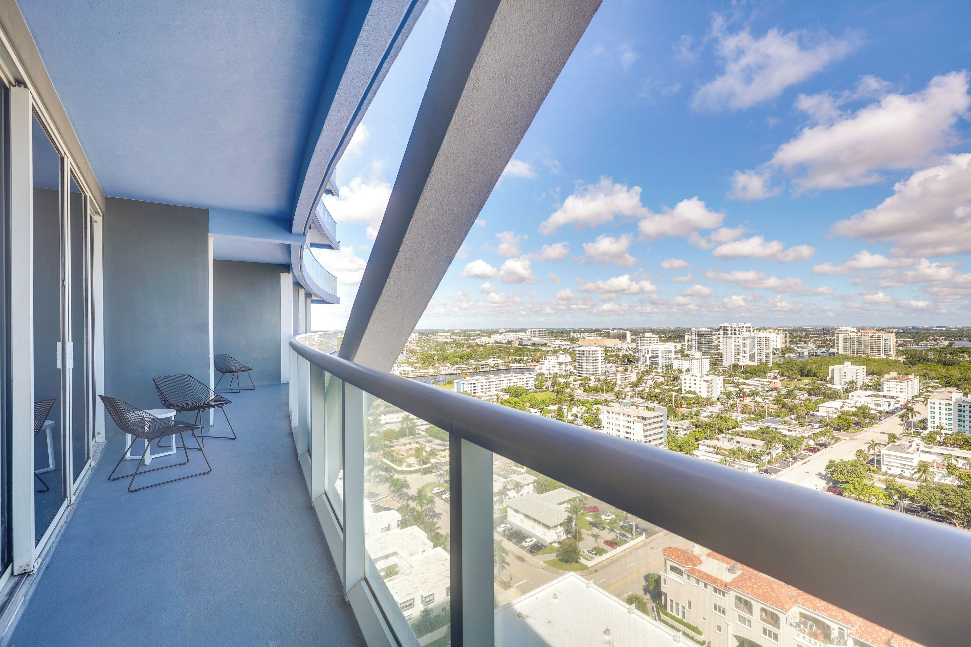 A balcony with a city view, glass railings, and outdoor seating.