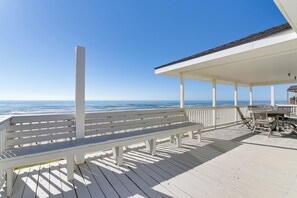 Eine Holzterrasse mit einer weißen Bank und einem Tisch mit Stühlen, mit Blick auf den Ozean.