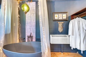 A bathroom with a freestanding bathtub, a towel rack with a white towel, a framed picture on the wall, and a wall-mounted air conditioner. - Grill & Rooftop Deck: Cozy Hideaway in Garfield (Garfield)