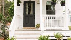 A white house with a black door, number 422, and a porch with potted plants.
