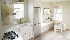 A modern kitchen with white cabinetry, a stainless steel refrigerator, a gas stove, and a dining area with a wooden table and white chairs.