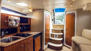 A compact kitchen with a coffee maker, microwave, and stove. There is a small sink and wooden cabinets. A staircase leads to a seating area with a view outside. - A romantic night for couples in the yacht in Marina del Rey, Los Angeles (Marina del Rey)