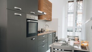 A modern kitchen with grey cabinets, a built-in oven, and a wooden upper cabinet. There is a dining table with chairs and a coffee maker.