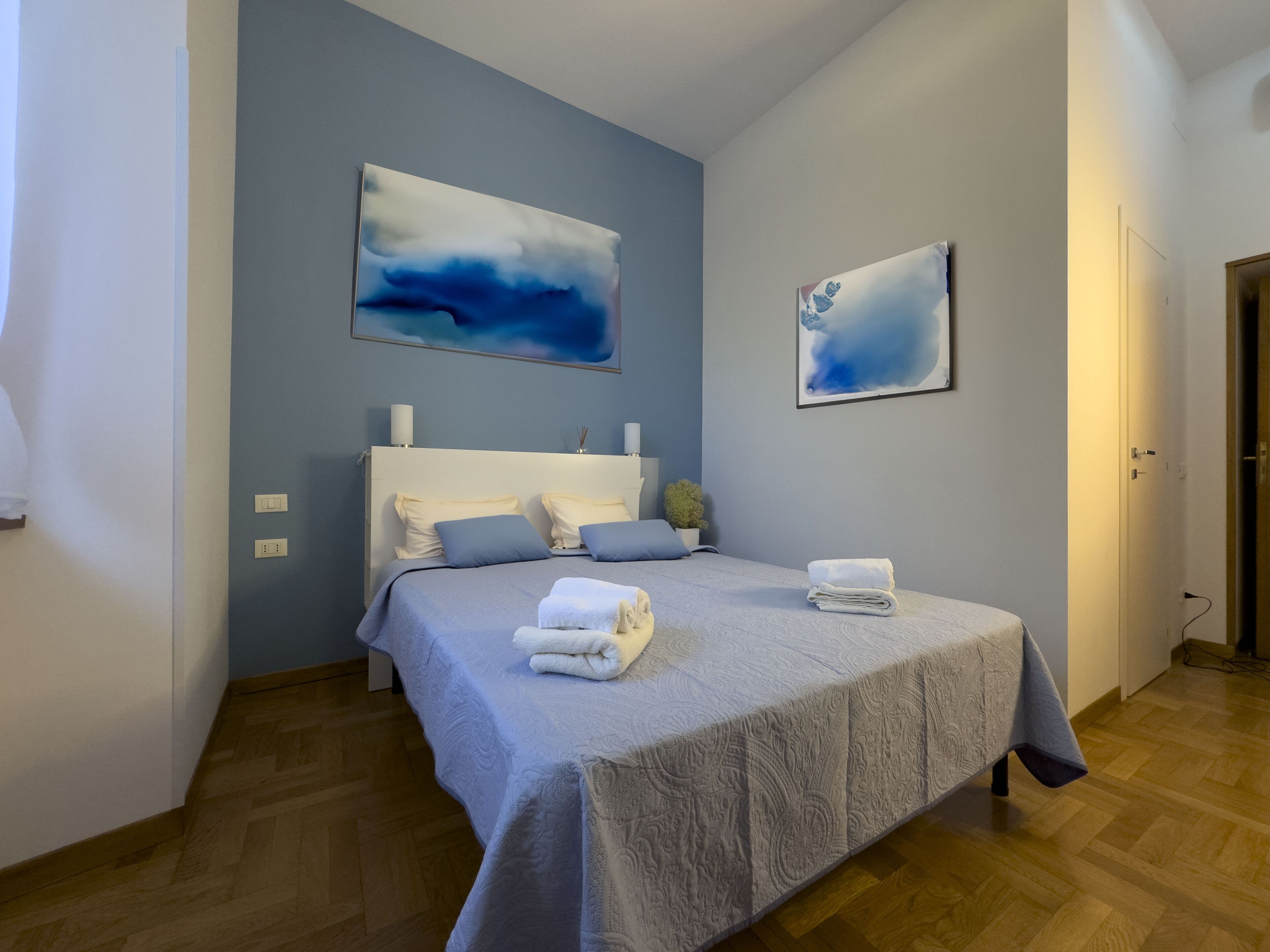 A bedroom with a bed, pillows, a bedside table, and two wall-mounted paintings.