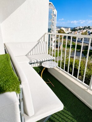 A balcony with a white sofa, a small round table, and a view of a cityscape.