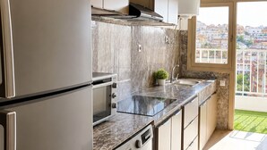 A modern kitchen with stainless steel appliances, a built-in washing machine, and a view of the city. - Tangier Center 3BR - Balcony, AC, Netflix & Wi-Fi (Tangier)