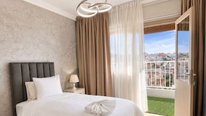 A bedroom with a bed, a nightstand, a lamp, and a view of a cityscape through a balcony. - Tangier Center 3BR - Balcony, AC, Netflix & Wi-Fi (Tangier)