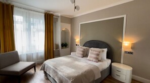 Ein Schlafzimmer mit einem Bett, Nachttischen, einem Sessel und einem Fenster mit Vorhängen.