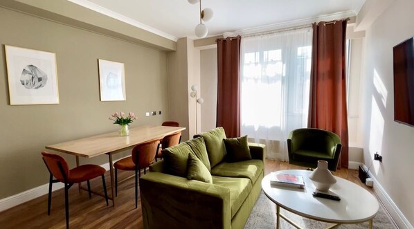 Una sala de estar con un sofá verde, una mesa de comedor de madera y un sillón verde.