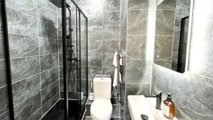 A modern bathroom with a glass-enclosed shower, a white toilet, and a sink with a mirror.