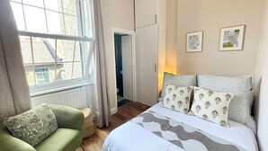 A bedroom with a bed, a green armchair, a window, and a door leading to another room.