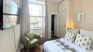 A bedroom with a bed, a green armchair, a window, and a TV mounted on the wall.