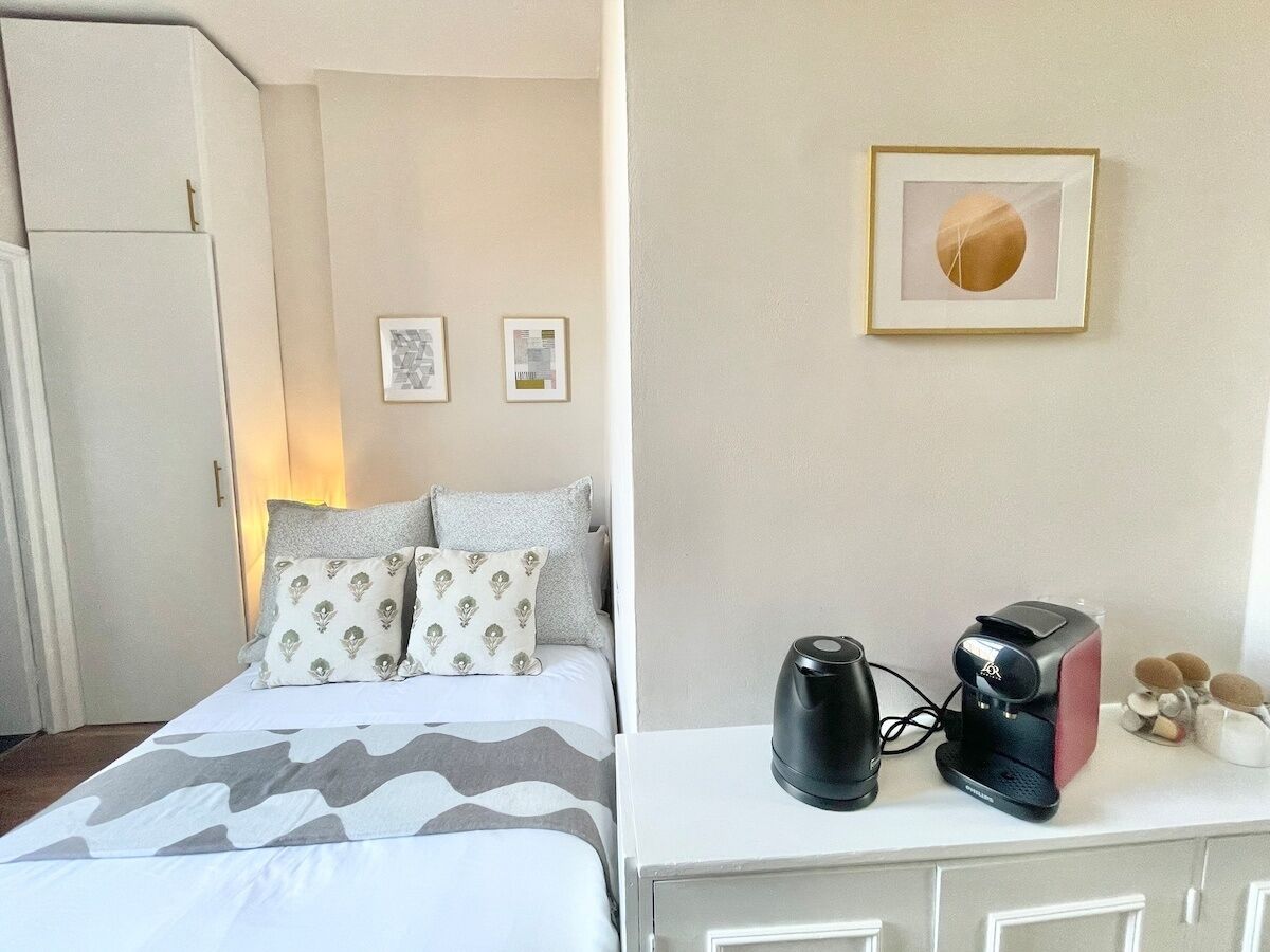 Een hotelkamer met een bed, kussens, een koffiezetapparaat en een ingelijste foto aan de muur.