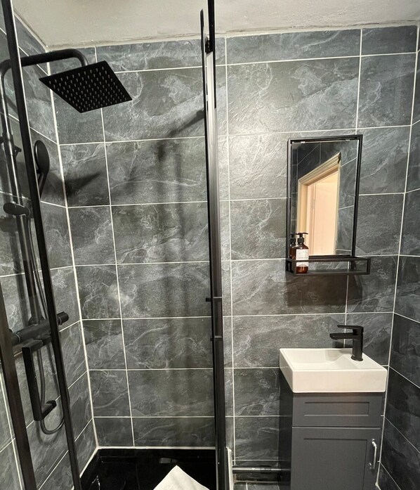 A modern bathroom with a glass shower enclosure, a white sink, and a dark cabinet.