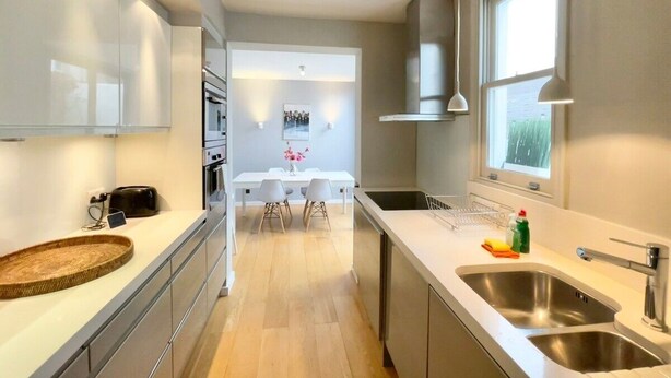 A modern kitchen with a central island, a dining area with chairs, and a large window providing natural light. - 2 bed Mews 2 minutes from Earls Court station (Greater London)