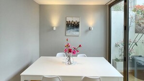 A modern dining area with a white table, two chairs, a vase with pink flowers, and a framed picture on the wall. - 2 bed Mews 2 minutes from Earls Court station (Greater London)