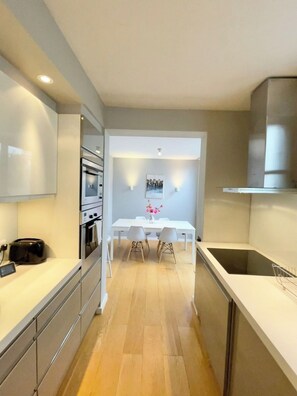 Uma cozinha moderna com eletrodomésticos embutidos, um espaço de refeições com mesa e cadeiras brancas e uma janela grande.