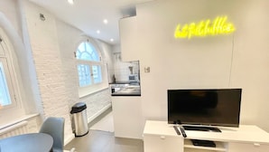 A modern living room with a flat-screen TV, a dining area, and a kitchen in the background. - Cozy 1 bedroom flat near Tower Bridge (Greater London)