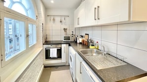 A modern kitchen with white cabinets, a built-in oven, a microwave, and a sink with a dish rack. - Cozy 1 bedroom flat near Tower Bridge (Greater London)