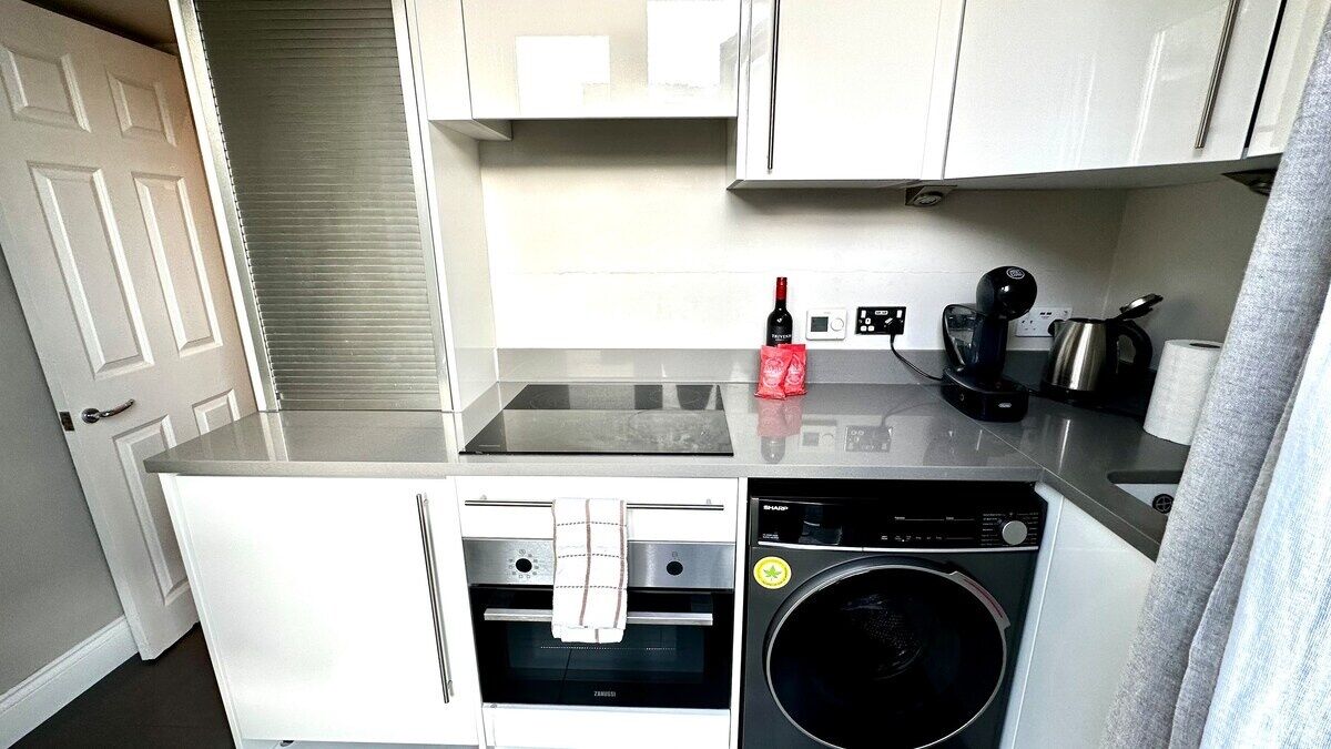Une petite cuisine équipée d’un lave-linge, d’une machine à café et d’une bouteille de vin.