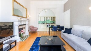 A living room with a fireplace, a television, a sofa, and a dining area with chairs. - Classy 2 bed apartment with high ceilings (Greater London)