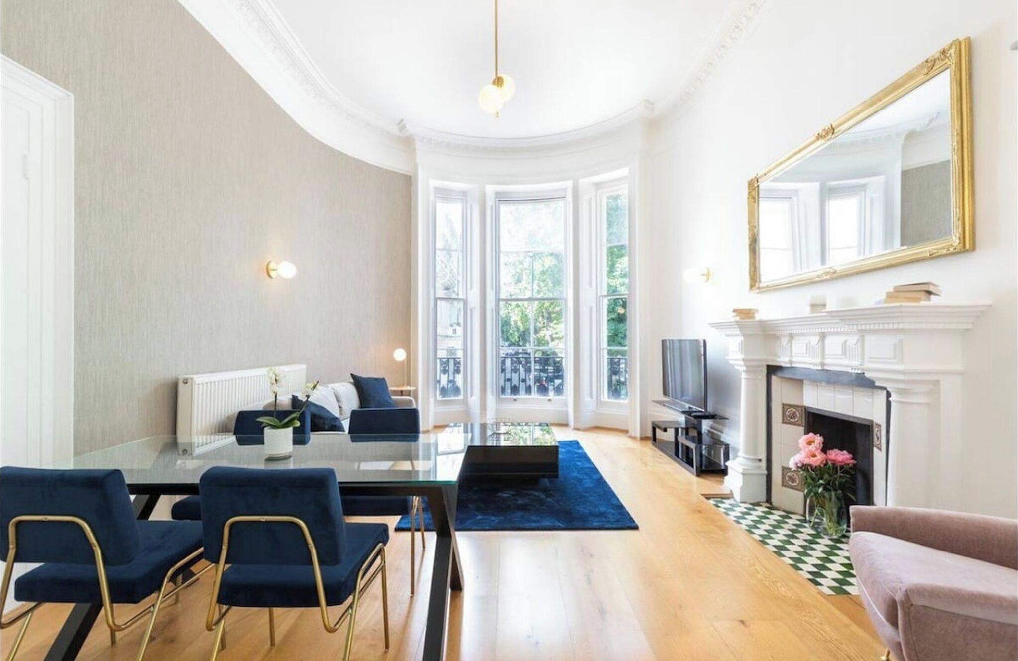 Een ruime woonkamer met een open haard, een eethoek met een glazen tafel en een groot raam met uitzicht op groen.