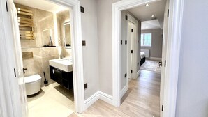A modern interior with a bathroom featuring a toilet, sink, and mirror. There are wooden floors and white walls. - Lux Top floor 3 Bed Flat near Marble Arch (Greater London)