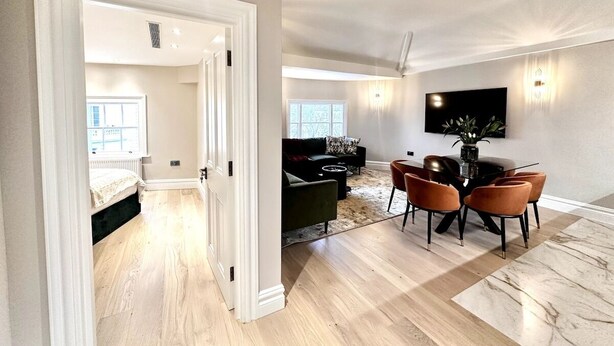 A modern living room with a dining area, hardwood flooring, a black sofa, and a TV mounted on the wall. - Lux Top floor 3 Bed Flat near Marble Arch (Greater London)