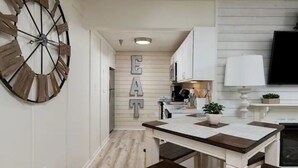 Eine Küche mit einer großen Holz-Standuhr, weißen Schränken und dem Wort 'EAT' an der Wand.