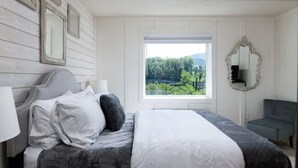Ein Schlafzimmer mit Bett, Fenster mit Aussicht, Spiegel und Stuhl.