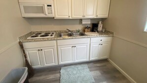 Een kleine keuken met witte kastjes, een magnetron, een fornuis en een spoelbak.