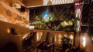 Un intérieur chaleureux avec un sol carrelé, un banc en bois, une petite table avec une lampe et diverses plantes en pot.
