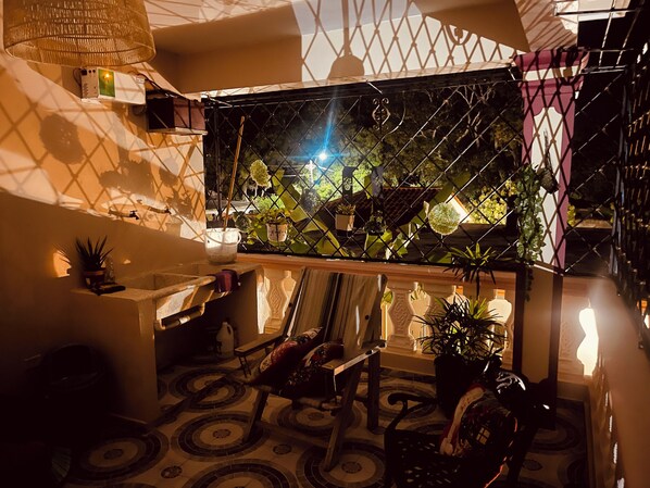 A cozy interior with a tiled floor, a wooden bench, a small table with a lamp, and various potted plants.