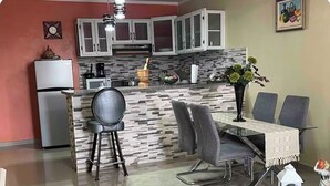 Une cuisine moderne avec des meubles blancs, un îlot central doté de tabourets et une table à manger avec des chaises.
