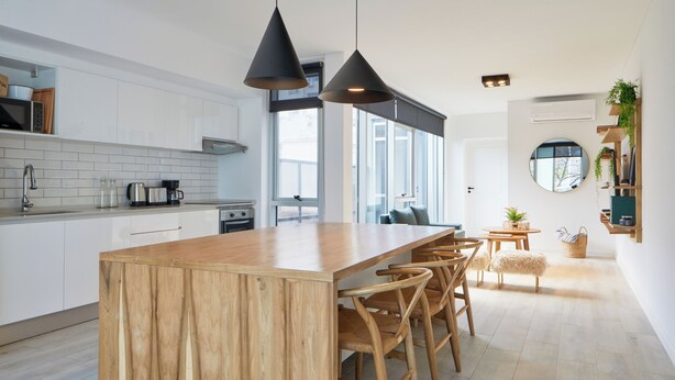 Una cocina moderna con isla de madera, armarios blancos e iluminación colgante.