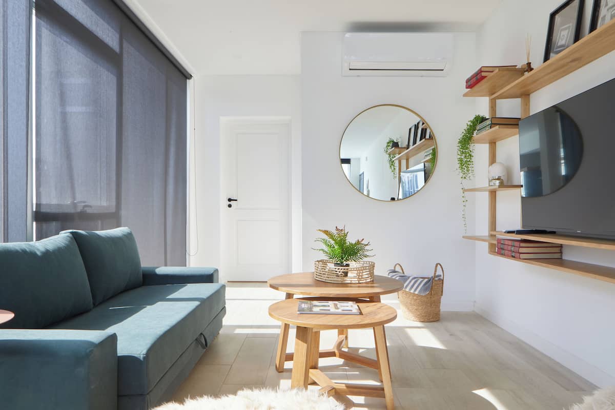 A modern living room with a sofa, two wooden tables, a round mirror, and shelves with books and decorative items.