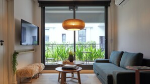 Una sala moderna con un sofá, una mesa de centro, un televisor montado en la pared y vistas a un balcón con plantas.