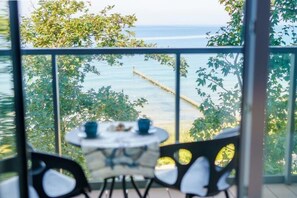 Ein Balkon mit Tisch und Stühlen, mit Blick auf ein Gewässer und Bäume.