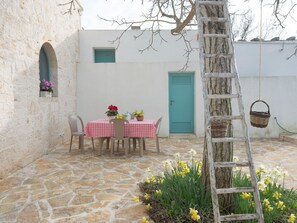 A stone-floored patio with a table set for two, a wooden ladder, and a door in the background. - Trulli-style Chalet Near Forest Walks (Locorotondo)