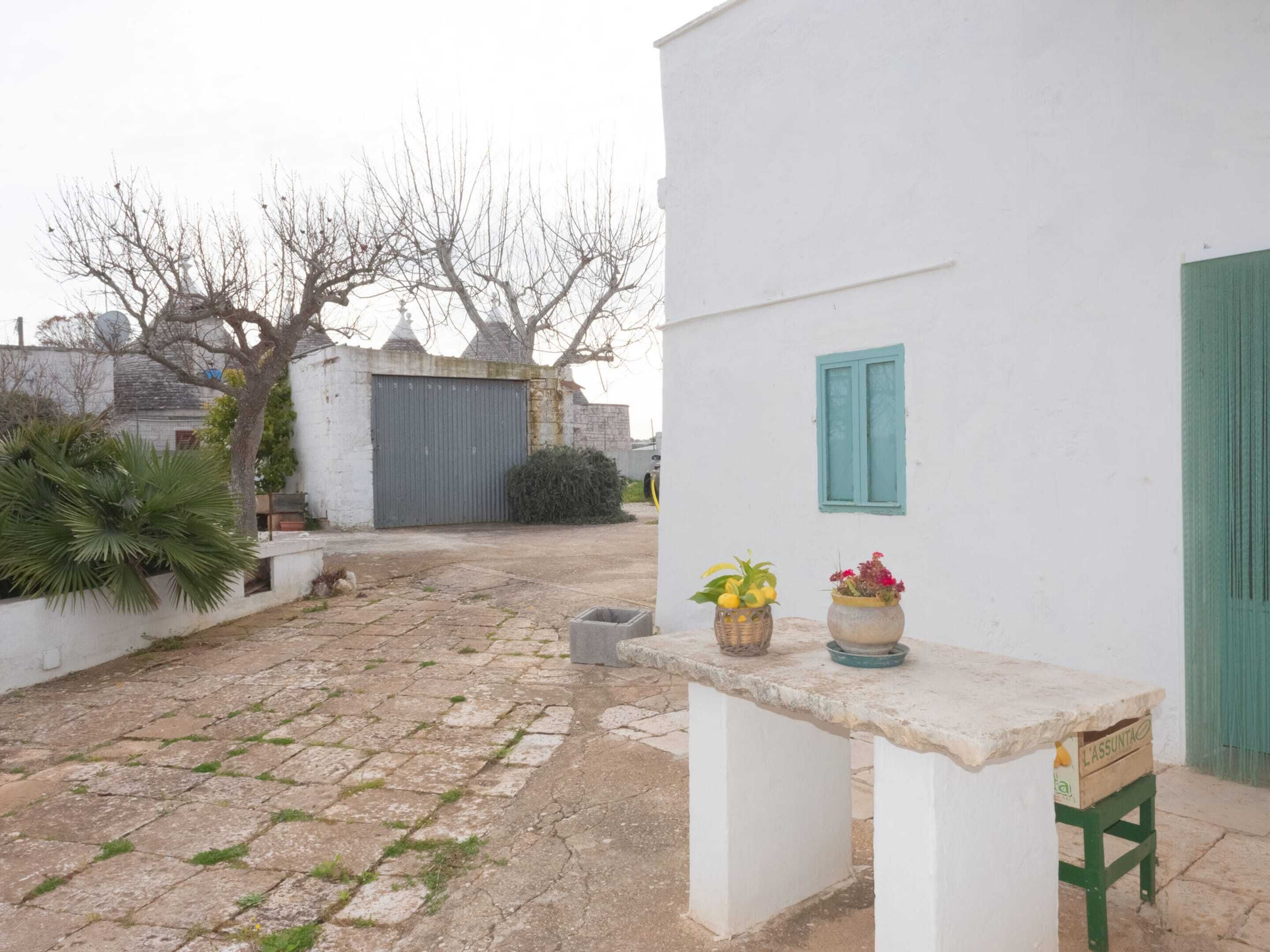 Un cortile con un edificio bianco, un pavimento in pietra e un tavolino con piante in vaso.