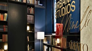 A library with bookshelves, two chairs, a lamp, and a wall with 'URBANY STUDIO' and 'Ninelli' text. - Schone Wohnung mit Aufzug (Trieste)