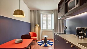 A compact kitchen with modern appliances, a dining area with a red table and chairs, and a view of the outside through a window with curtains. - Schone Wohnung mit Aufzug (Trieste)