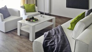 A modern living room with a white sofa, a coffee table, and a dining table set with food. - Appartements am Heidensee in Schwerin (Schwerin)