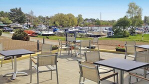 An outdoor patio area with metal tables and chairs, overlooking a marina with boats. - Appartements am Heidensee in Schwerin (Schwerin)