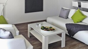 A modern living room with a white sofa, a white coffee table, and a dining area with a blackboard on the wall. - Appartements am Heidensee in Schwerin (Schwerin)